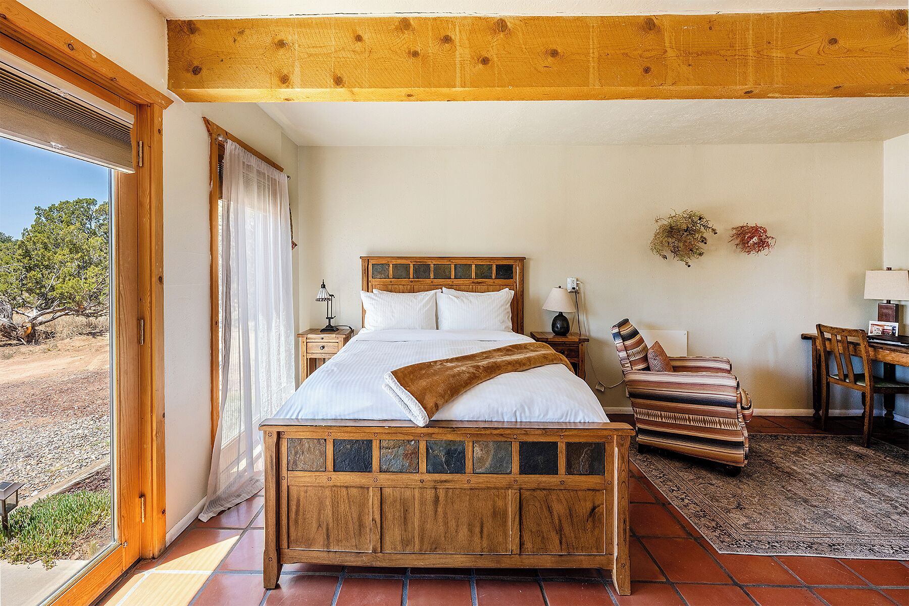 Une chambre à coucher avec un lit en bois, une table de chevet, une chaise, un bureau et une vue sur l’extérieur.
