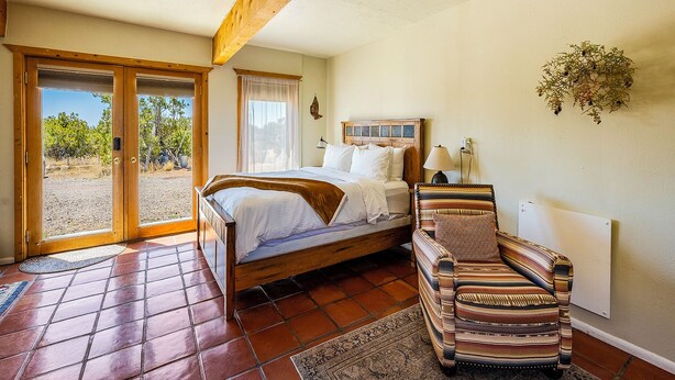 Ein Schlafzimmer mit Bett, Stuhl, Fenster und Tür, die zu einem Außenbereich führt.