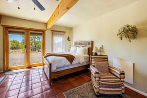 A bedroom with a bed, a chair, a window, and a door leading to an outdoor area.