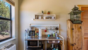 Eine kompakte Küche mit Einbauofen, Mikrowelle und Kaffeemaschine, einem kleinen Fenster und einem Holzkorpus.