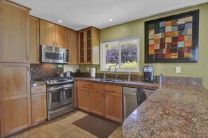 Enjoy cooking in this well-equipped kitchen with a microwave, stove, and granite countertop, offering a view of lush greenery.