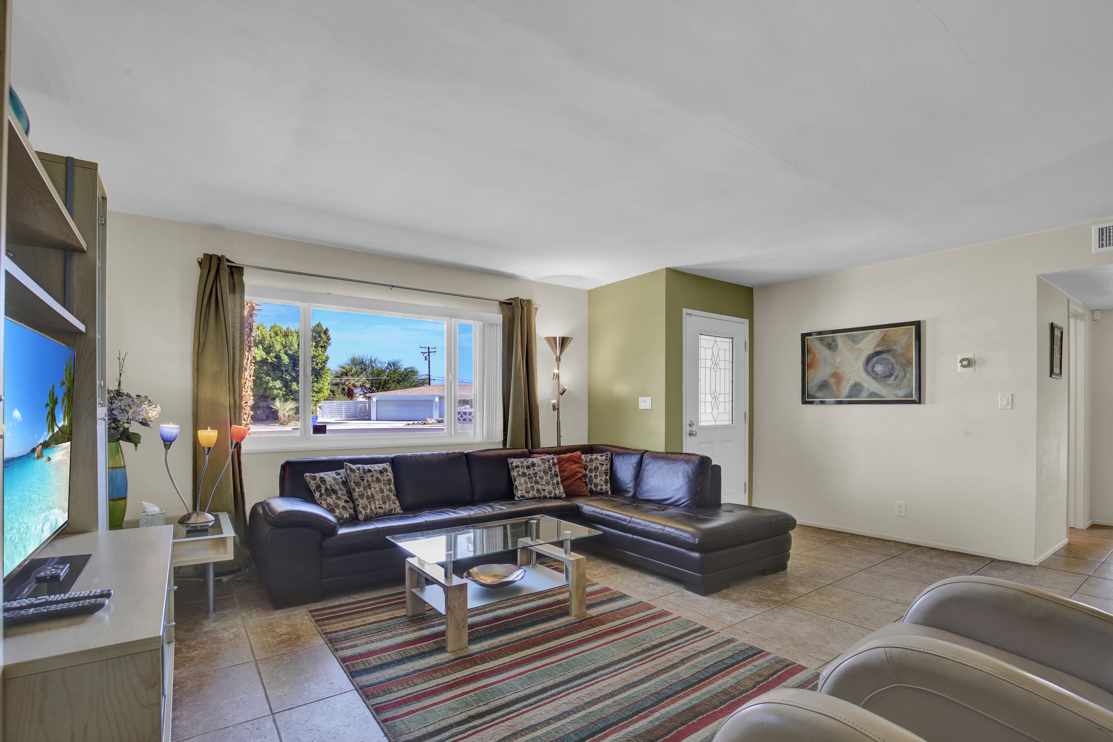 A living room with a sectional sofa, a glass coffee table, a TV, and a painting on the wall.