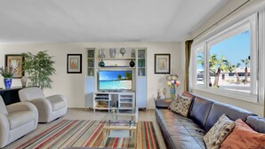 A living room with a large TV, a sofa, a coffee table, and a bookshelf.