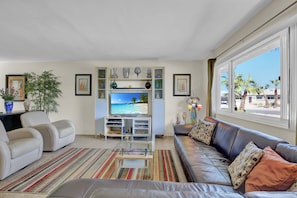 Relax in a stylish living room with a leather sofa, armchair, and flat-screen TV, offering a view of palm trees and the beach.