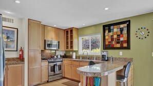 A modern kitchen with wooden cabinets, stainless steel appliances, a granite countertop, and a colorful abstract painting on the wall.