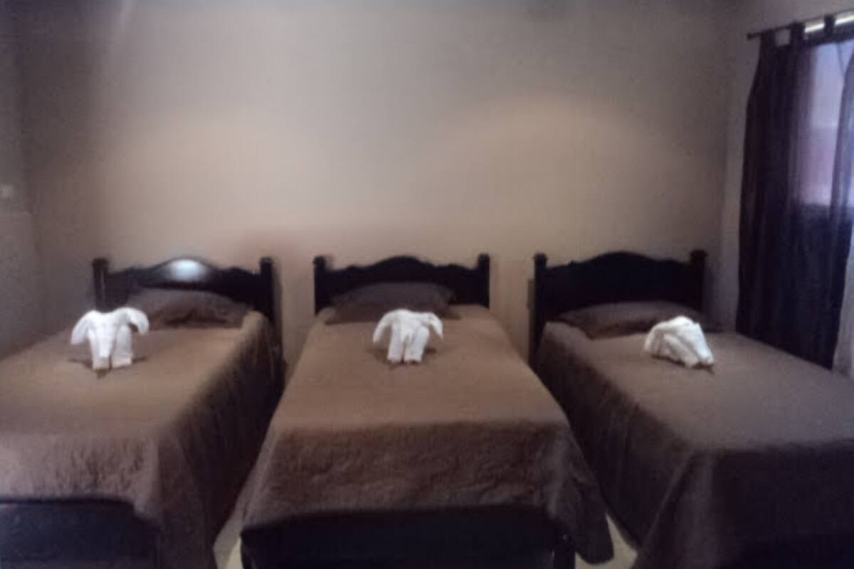Une chambre avec trois lits simples, chacun étant muni d’une serviette blanche posée sur le lit.