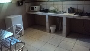 A compact kitchen with a microwave, sink, and stove. There is a chair and a small trash bin. - Casa Maya (Monteverde)