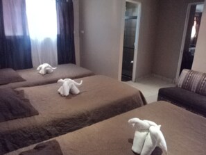 A hotel room with three beds, each with a brown bedspread and a white towel. There is a sofa and a door leading to a hallway. - Casa Maya (Monteverde)