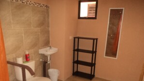 A bathroom with a toilet, sink, and a black shelf unit. - Casa Maya (Monteverde)