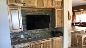 A kitchen with wooden cabinets, a stone backsplash, and a flat-screen TV mounted above the counter. - September Dates Open! Year Round Fun For The Whole Family! Municipal Utilities (Honeoye)