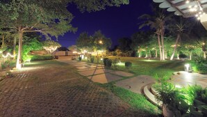Un espace extérieur aménagé pour la nuit, avec un chemin pavé, des arbres et des éclairages décoratifs.