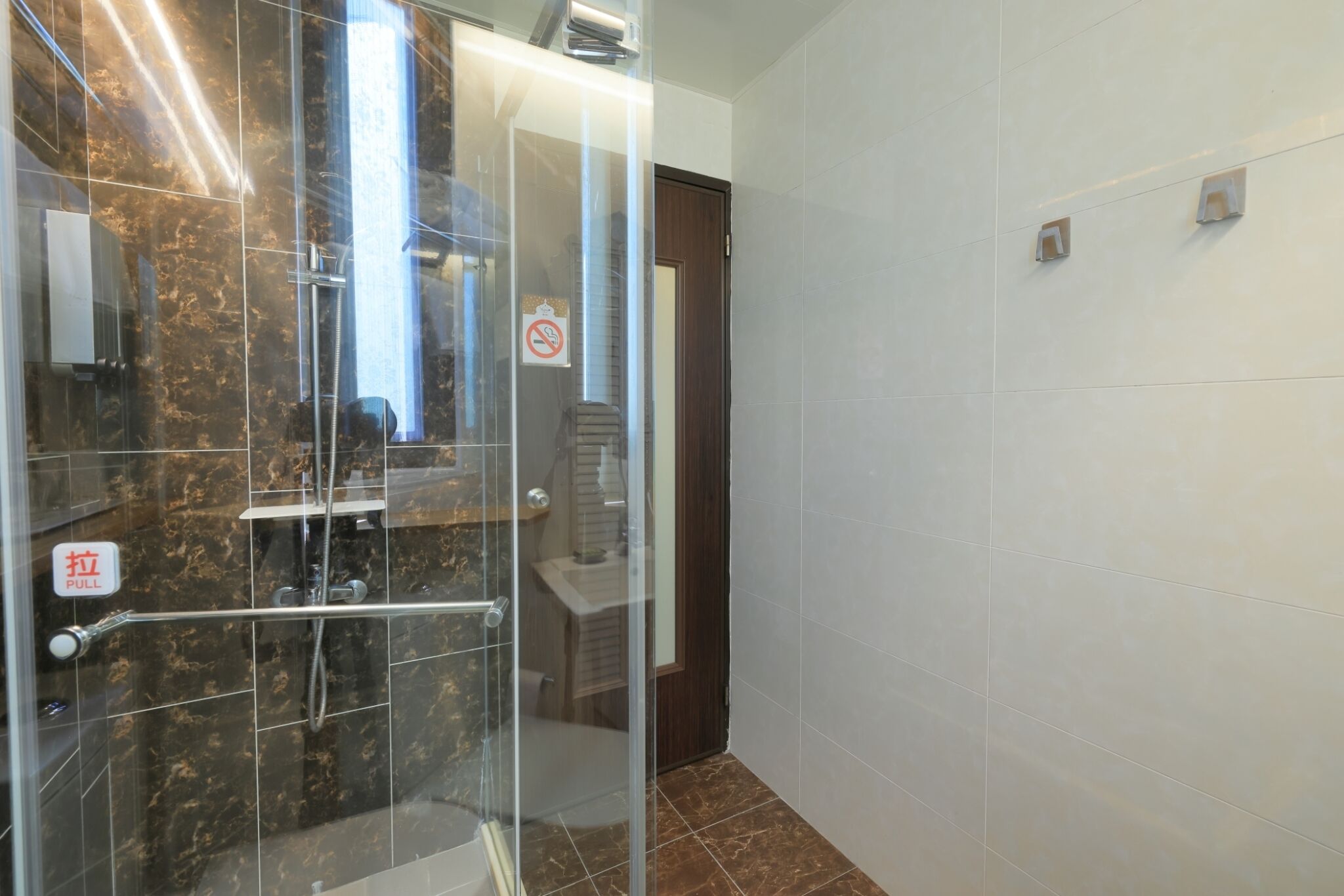 Een badkamer met een douchecabine van glas, een bord met 'TREK', een rookverbodsgevaarte en een deur naar een andere kamer.