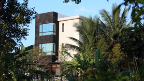 Un bâtiment moderne à deux étages, doté de grandes fenêtres et d’un toit plat, entouré d’une végétation tropicale luxuriante.