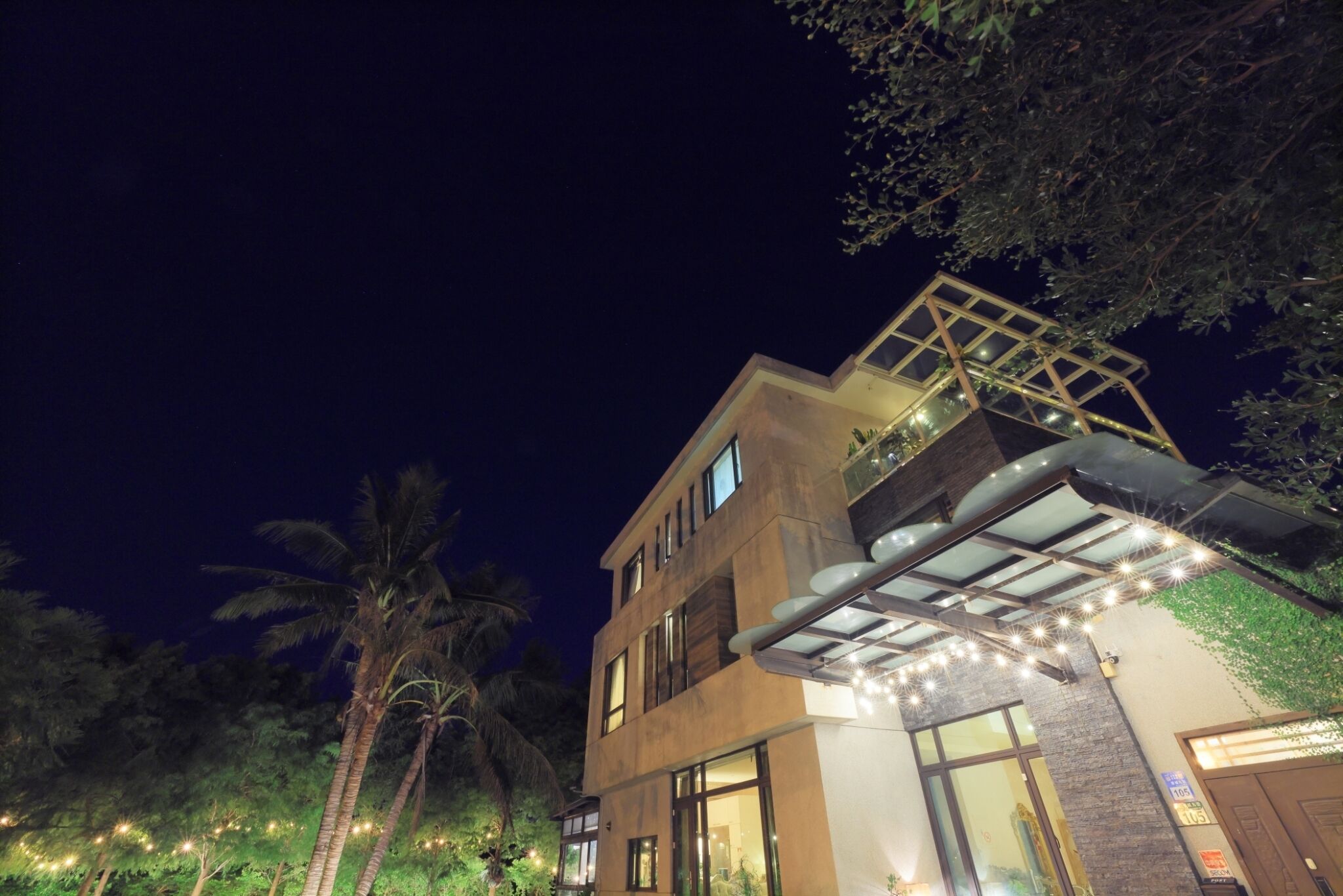A modern building with a glass facade, large windows, and a balcony with string lights.