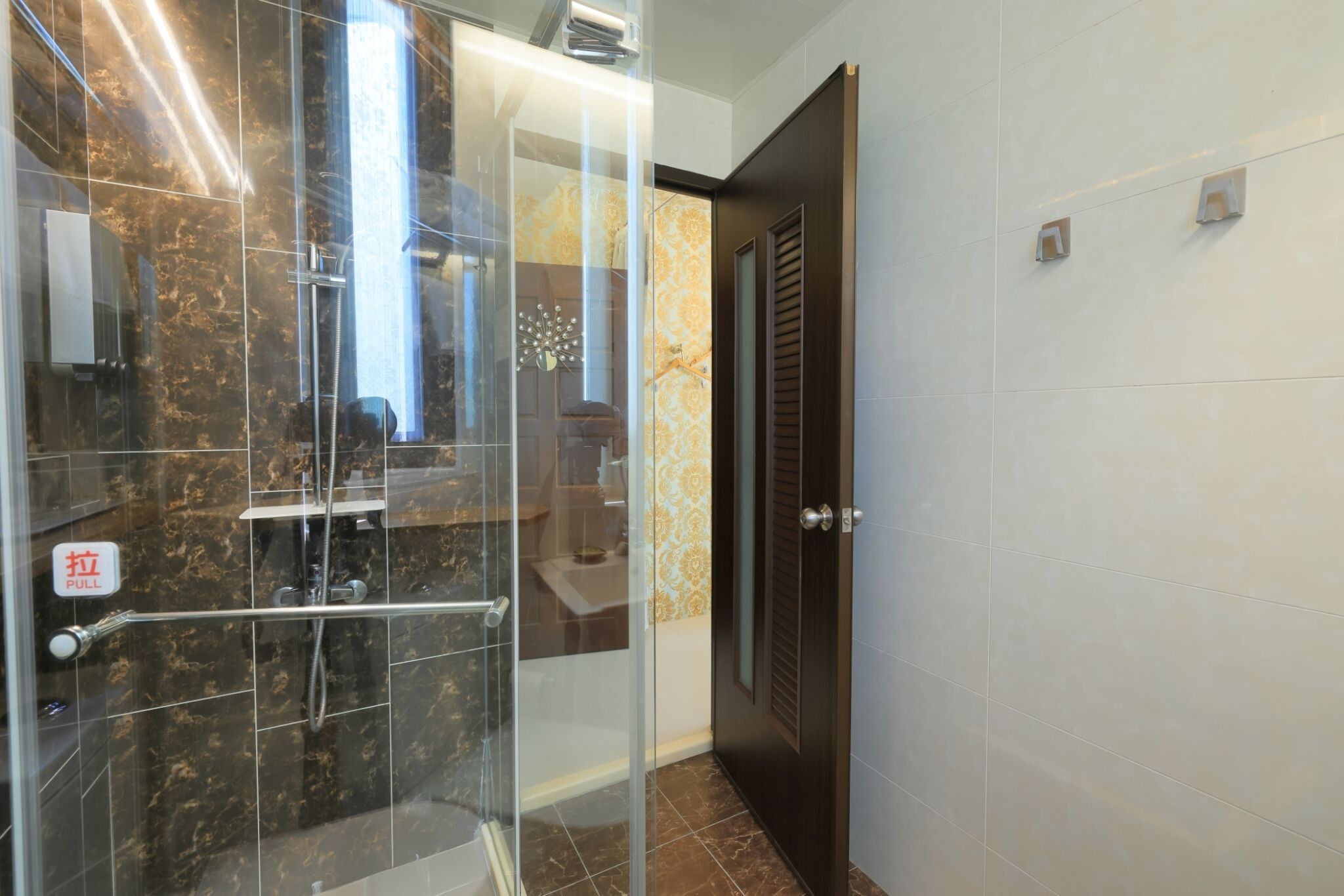 A bathroom with a glass shower enclosure, a towel rack, and a door with a pull handle.