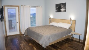Une chambre à coucher avec un lit en bois, une vue sur l’extérieur par une fenêtre et un tableau accroché au mur.