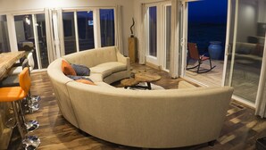 Un canapé incurvé agrémenté de plusieurs coussins, une table basse en bois et un coin repas avec des chaises.