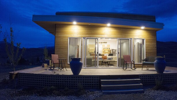 Une maison moderne avec une façade en bois, de grandes portes-fenêtres coulissantes et une terrasse aménagée avec du mobilier d’extérieur.