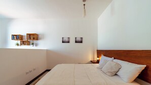 Un dormitorio ordenado con una cama grande, cabecera de madera, mesitas de noche y estanterías en la pared con libros y plantas.