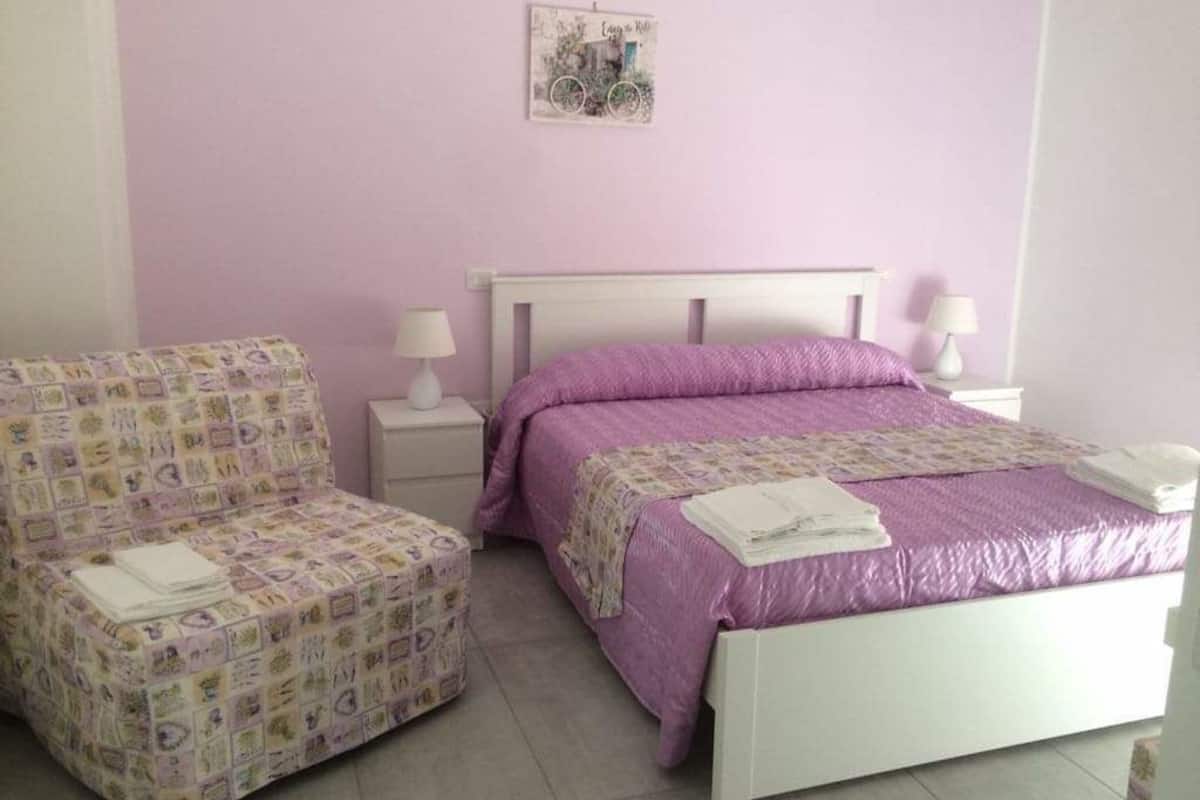 A bedroom with a bed, a chair, two bedside tables, and a wall decoration.