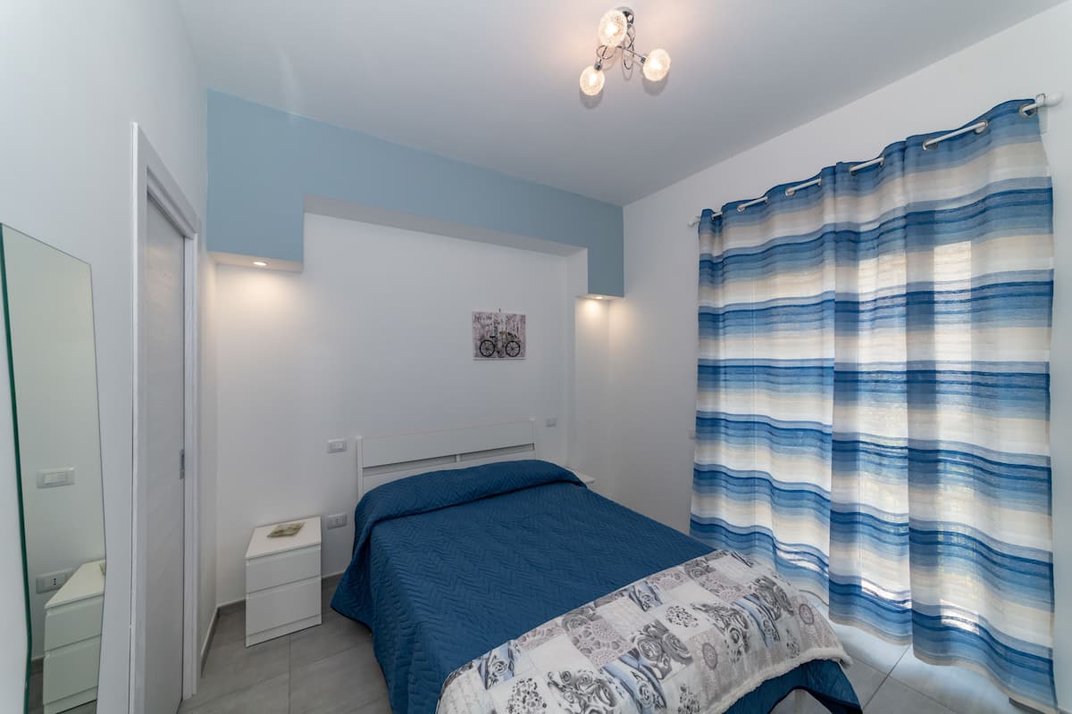 A bedroom with a bed, a nightstand, a mirror, and a wall-mounted light fixture.