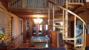 A log cabin interior with a pool table, a spiral staircase, and a leather couch.