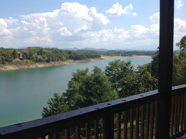 A view of a river from a wooden deck with a railing, surrounded by trees and hills in the background.