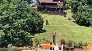 A cabin with a deck overlooking a lake, surrounded by dense forest.
