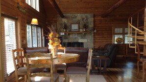 A cozy cabin interior with a stone fireplace, wooden furniture, and a spiral staircase.
