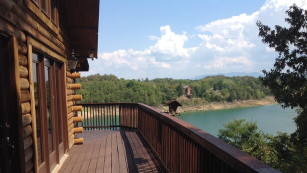 A wooden deck with a view of a lake and forested hills.
