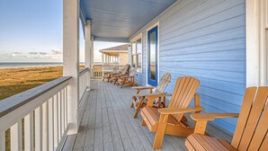 Una terraza de madera con sillas y una mesa, con vista a la playa.