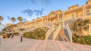Un hotel frente a la playa con varios balcones, una escalera central y palmeras.
