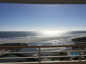 A balcony with a view of a beach and a swimming pool.