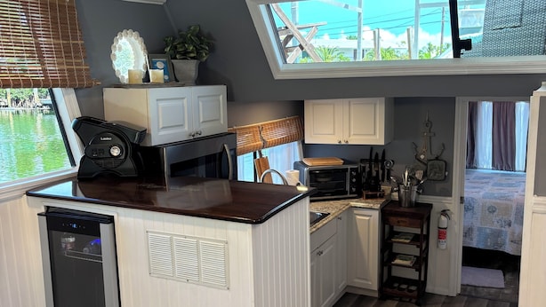 A compact kitchen with a dishwasher, a microwave, and a sink. There is a window with a view of the outdoors, and a ceiling fan. - Fla Keys Luxury Houseboat, Prime Location-Steps to Fun, Food & Water Adventures (Tavernier)