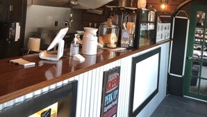 A coffee shop interior with a wooden counter, a coffee machine, and a display case with pastries. - Fla Keys Luxury Houseboat, Prime Location-Steps to Fun, Food & Water Adventures (Tavernier)