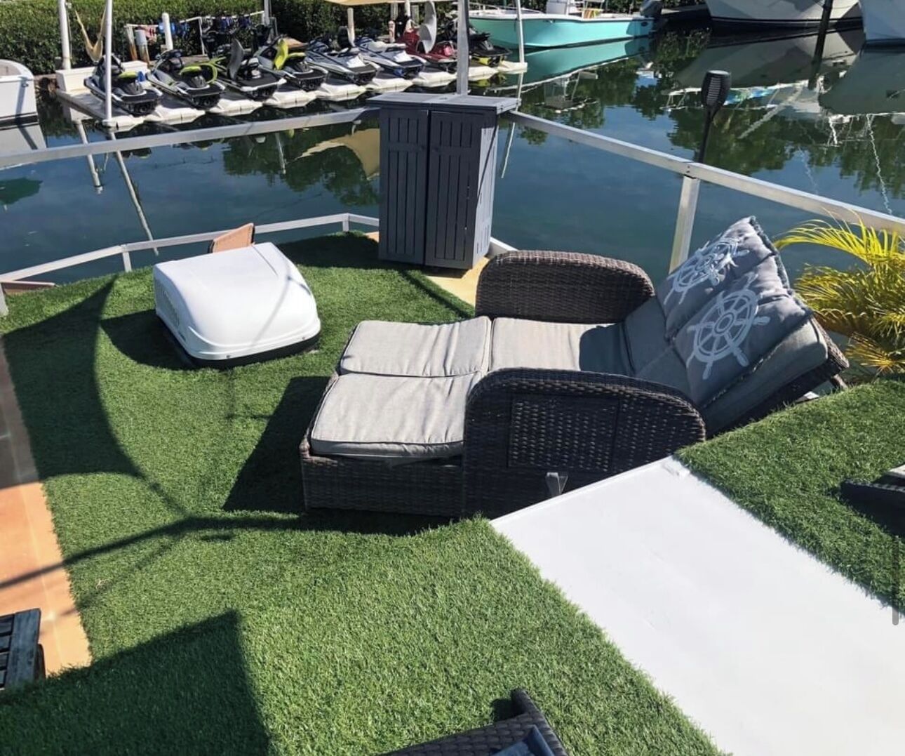 A poolside area with artificial grass, a wicker sofa, and a white lounge chair.