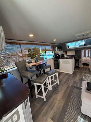 Een moderne keuken met een centraal eiland, een eethoek met tafel en stoelen, en uitzicht op het groen door grote ramen.