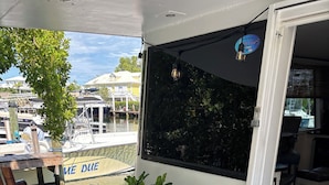 A balcony with a view of a marina, a wooden chair, a potted plant, and a welcome mat. - Fla Keys Luxury Houseboat, Prime Location-Steps to Fun, Food & Water Adventures (Tavernier)