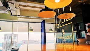 A modern interior with large windows, a view of a cityscape, and a counter with a sign reading "Suasana Suites cafe." - JB Town Executive Suite (Johor Bahru)