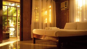 A bedroom with a bed, curtains, and a window with a view of greenery. - Don Remegio Villas (General Luna)