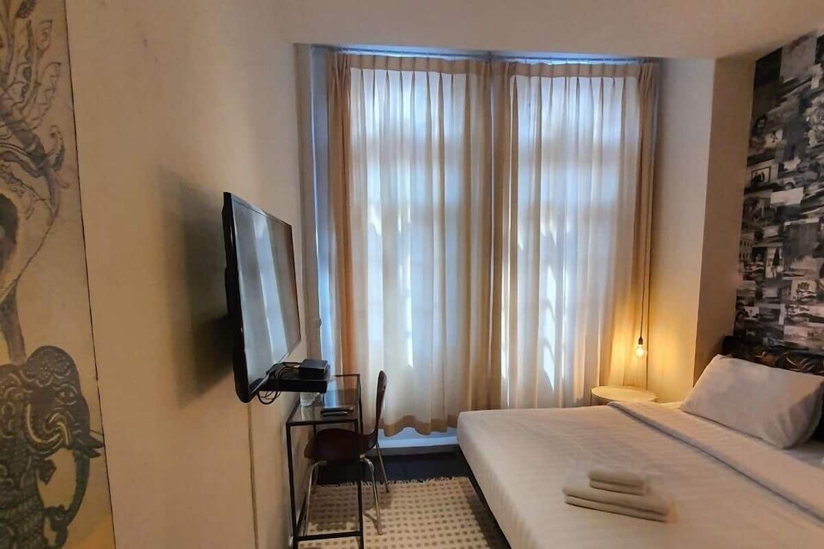 A hotel room with a bed, a desk with a chair, a television, and a window with curtains.