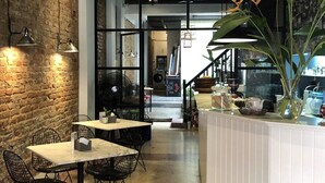 Un interior con paredes de ladrillo visto, una zona de bar con mostrador blanco y una escalera que sube a otro nivel.