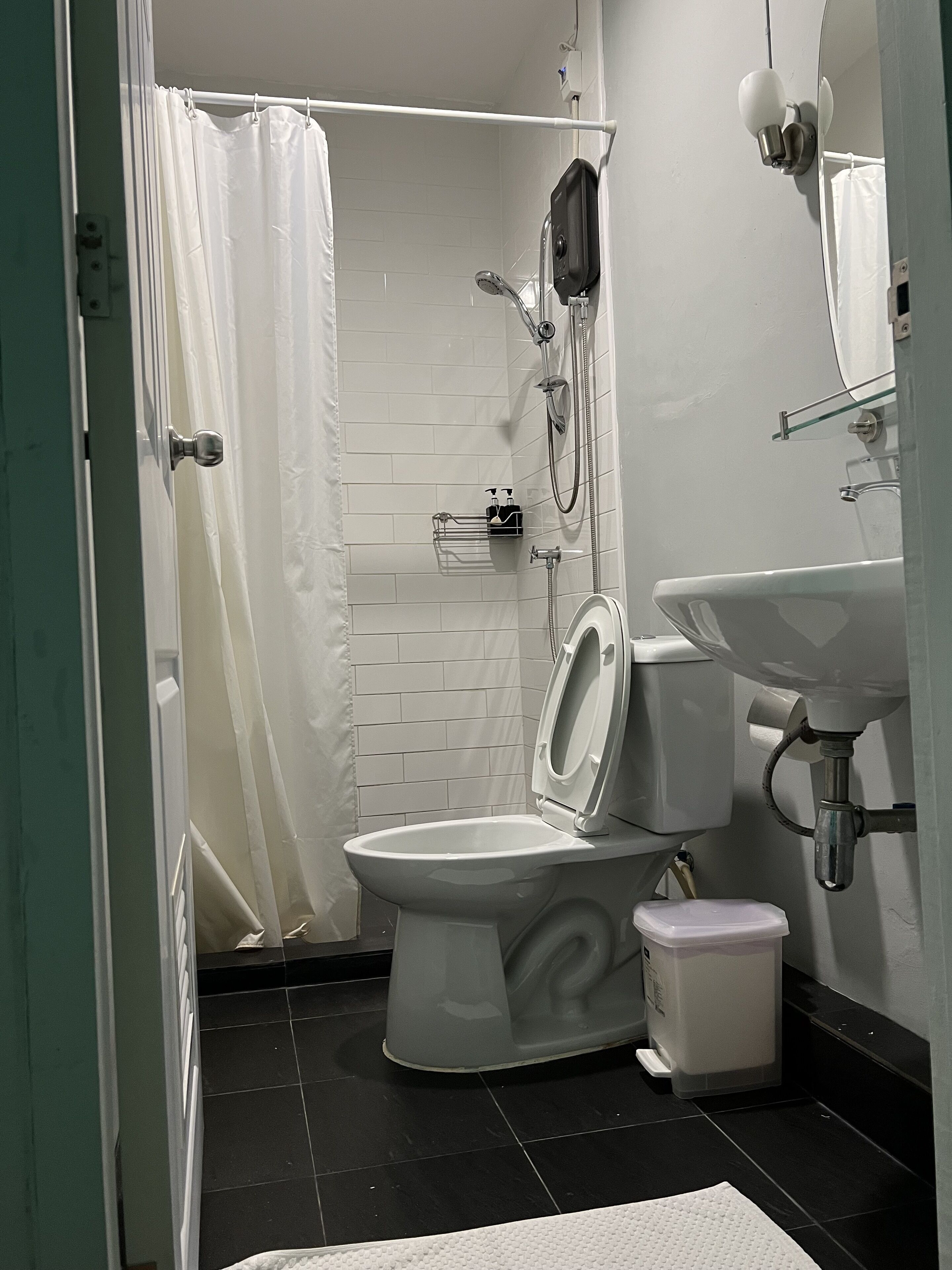 Un baño con inodoro, lavamanos, ducha y pared de azulejos blancos.