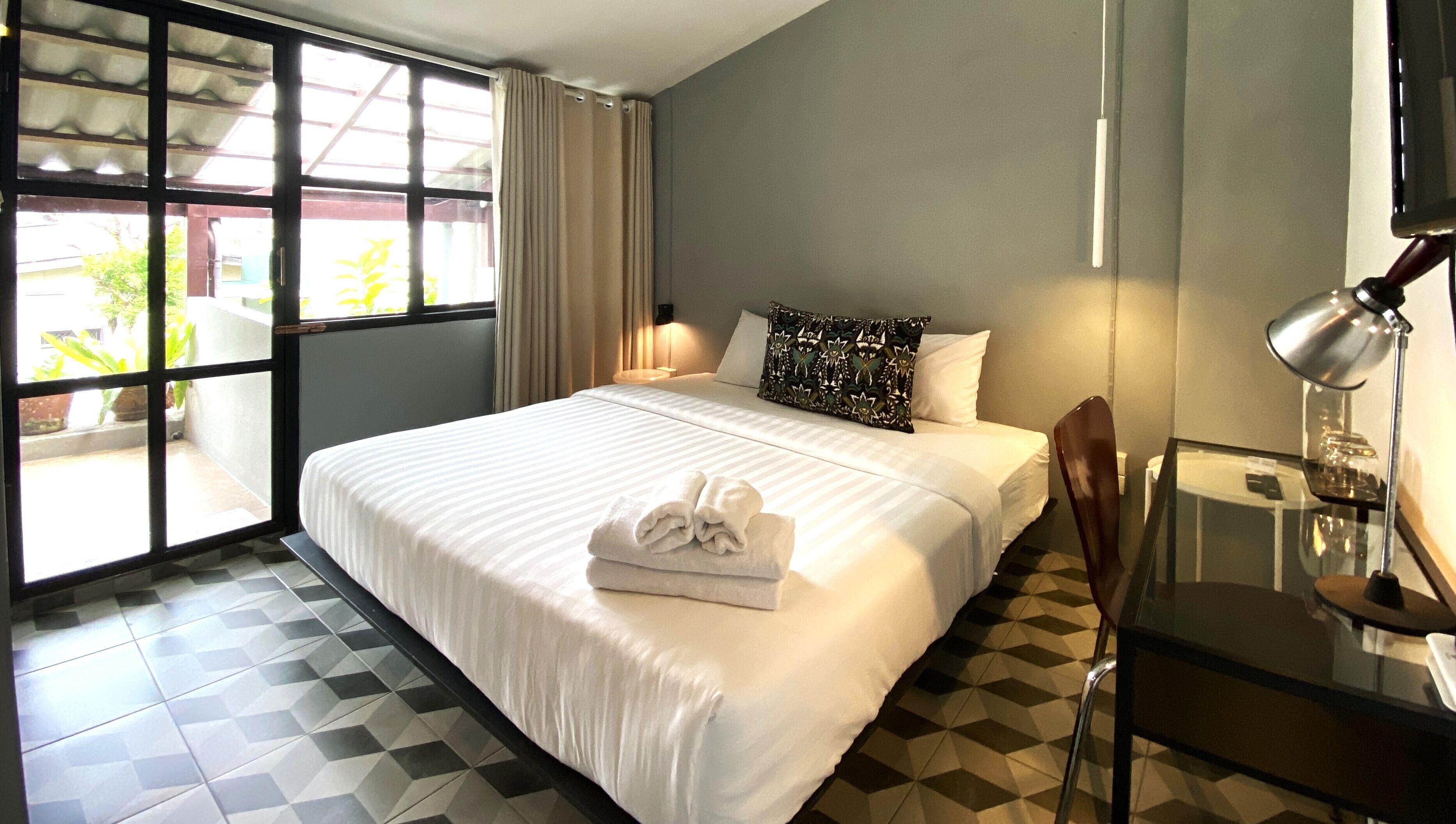 Una habitación de hotel con cama, una silla, un escritorio, una lámpara y una ventana con cortinas.