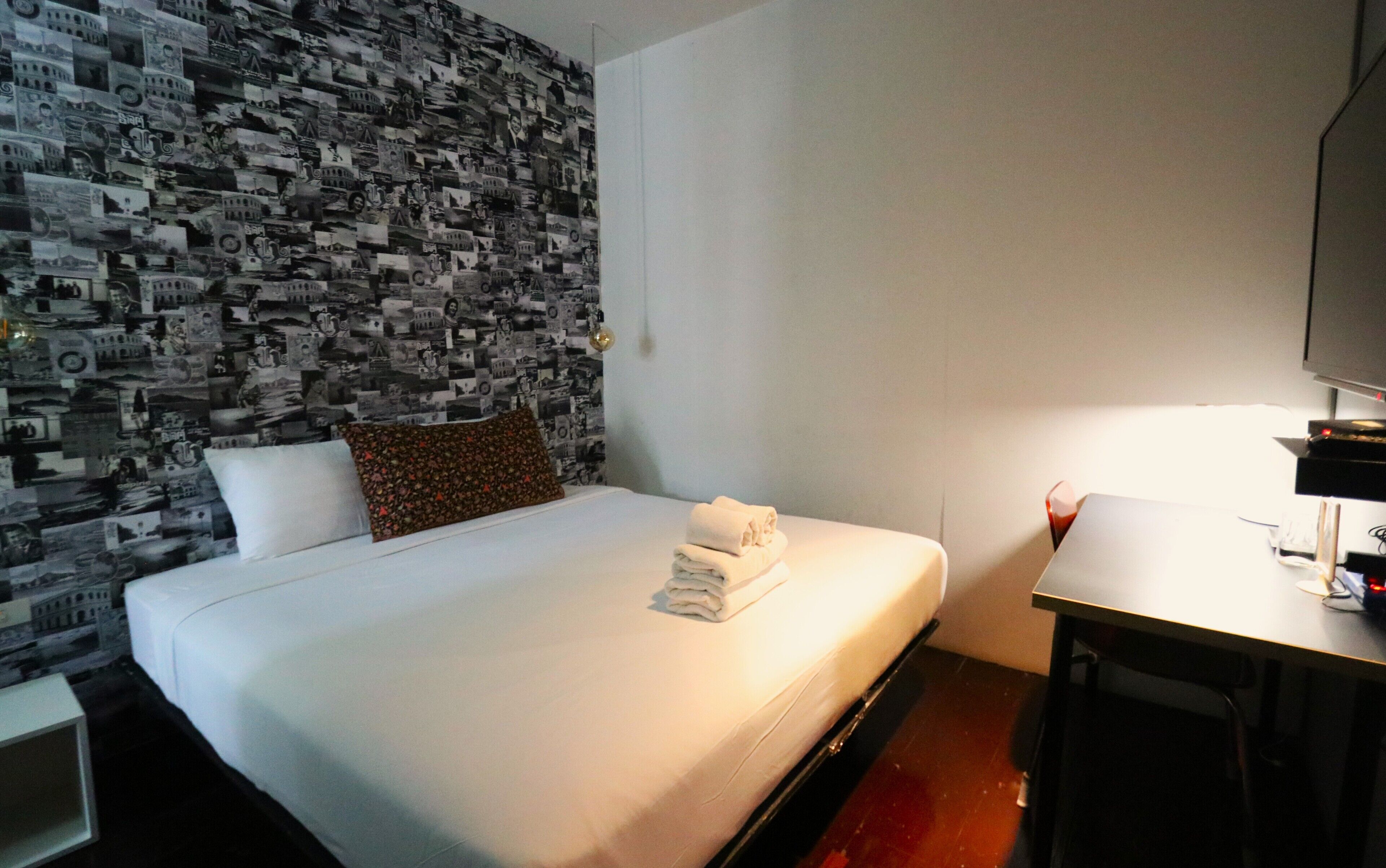 Habitación de hotel con una cama, un escritorio y una pared cubierta con un collage de fotografías en blanco y negro.