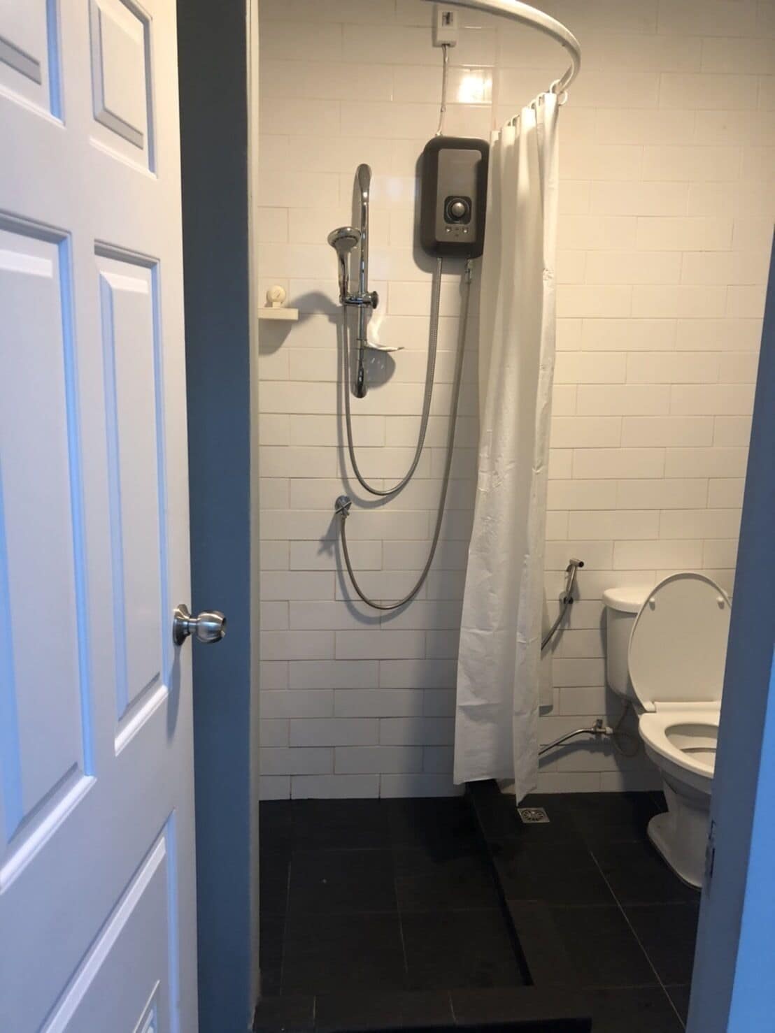 A small bathroom with a shower, toilet, and a door.