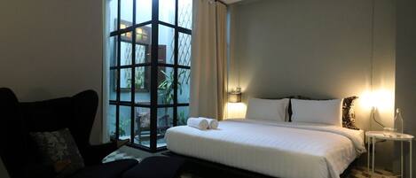 Une chambre d’hôtel avec un grand lit, une chaise, une petite table et une vue par la fenêtre.