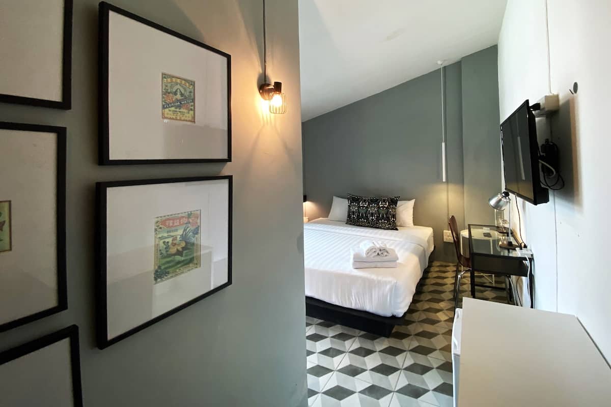 A hotel room with a bed, a desk, a TV, and framed pictures on the wall.