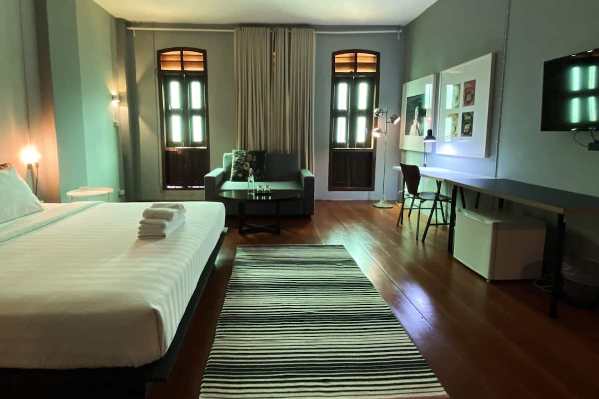 A hotel room with a large bed, a desk, a chair, a TV, and a window with curtains.
