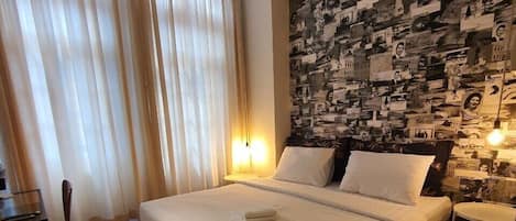 Une chambre d’hôtel avec un lit, un tapis à motifs, un mur orné d’un collage de photos et une fenêtre avec des rideaux.